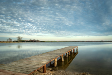 Long wooden bridge towards the lake and clouds on the sky