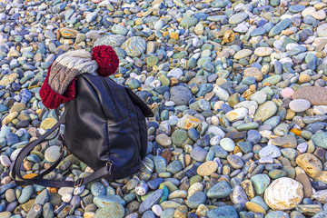 Women's backpack and winter hat on pebbles on the seashore. Tourism and Hiking concept