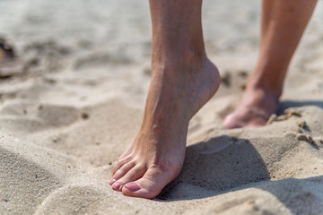 Fototapeta na wymiar female feet on sand at beach in summer in sunny weather