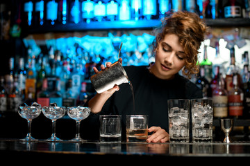barman lady pours the finished cocktail into glass.