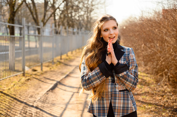 Naklejka premium Portrait of a stylish beautiful young girl with long hair with a smile in the park on the background of the road. Photo taken in sunny weather outdoors in spring.