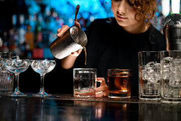 Close-up barman lady gently pours finished cocktail into glass.