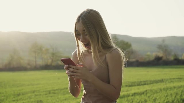 Funny attractive woman use smartphone field landscape cellphone happy mobile nature walk sunlight green girl smiling grass sunset portrait slow motion