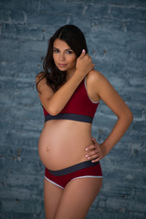 Fototapeta na wymiar Beautiful pregnant young athletic woman in sports maternity underwear against the background of a gray brick wall