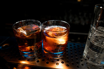 Close-up. Two glasses with cocktails like negroni or old fashioned stand at the bar.