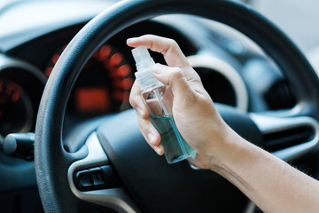 man hand spraying alcohol sanitizer on steering wheel in his car, against Novel coronavirus or...