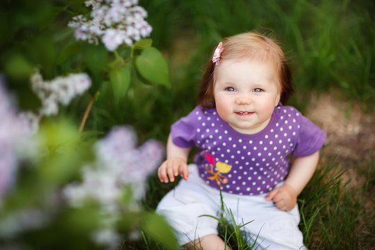 little girl crawling sitting in the grass at the lilac Bush, spring has come, cute baby, may, flowering