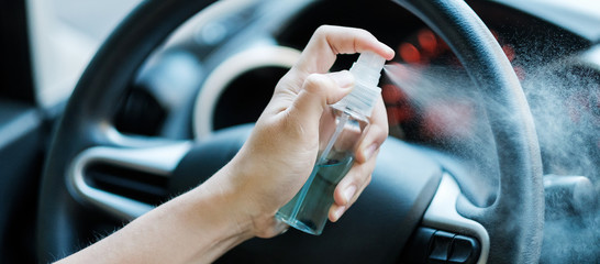 man hand spraying alcohol sanitizer on steering wheel in his car, against Novel coronavirus or...
