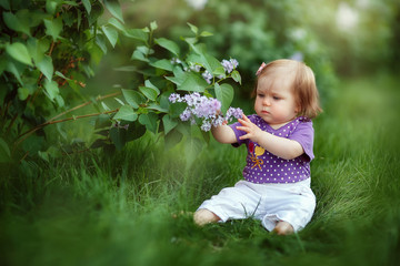 little girl crawling sitting in the grass at the lilac Bush, spring has come, cute baby, may, flowering