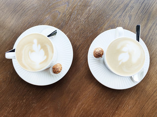 Two cups of cappuccino and chocolate sweets on a textured light wooden table in a cafe with modern trendy interior. Flat lay style. Copy space. Mockup for your design.