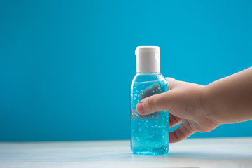 Child's hand holding a bottle of hand sanitizer gel. Hand hygiene as coronavirus protection. Antivirus and antibacterial product. Blue liquid with white round granules. Copy space for text