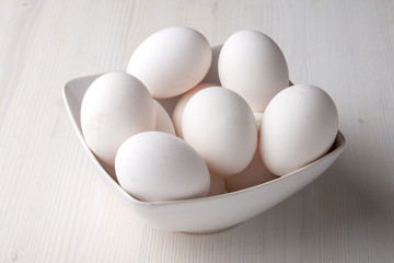Close-up of white eggs in a white bowl, with selective focus, on white wooden table horizontally, with copy space
