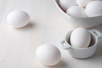 Top view of white eggs in a white bowls, with selective focus, on white wooden table horizontally, with copy space