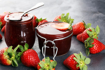 Strawberry jam in a glass jar with strawberries and leaves on rustic background. Homemade strawberry marmelade or jam