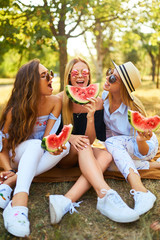 Three beautiful young girls have fun together and eating watermelon  in hot summer day. Friends...