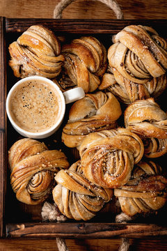 Traditional Swedish cardamom or cinnamon sweet buns Kanelbulle in wooden tray, cup of coffee on wooden table. Flat lay, space