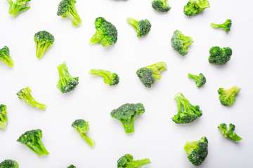 Fresh frozen broccoli pieces scattered over white background, top view