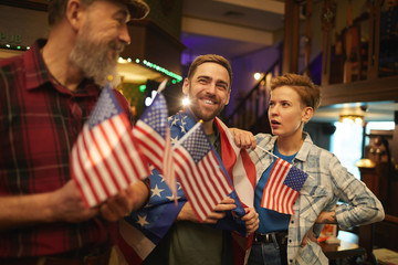 Group of people standing with American flags and discussing football match together in sport bar