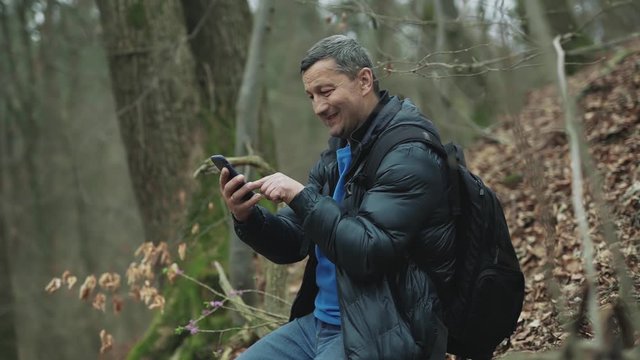 A man uses smarphone in the spring forest smile feel happy technology park cellphone autumn traveller tree telephone mobile phone casual close up slow motion