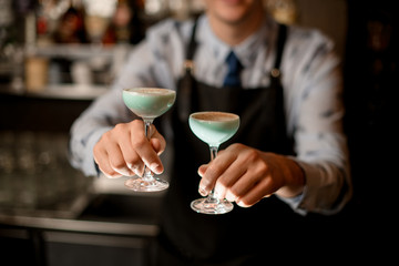 bartender's hands holding two glasses with blue cocktail
