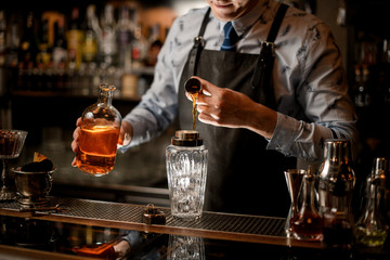 barman in black apron pours drink to glassy shaker using beaker.