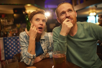 Young couple drinking beer and worried about their sport team while watching sport match in the bar