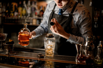 barman carefully pours drink to glassy shaker using beaker.