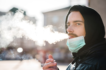 Smoking. Closeup man with mask during COVID-19 pandemic smoking a cigarette at the street. Smoking...