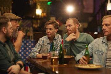 Group of friends sitting at the table talking to each other and drinking beer they have meeting in the bar