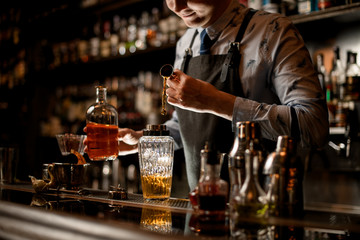 barman in black apron preparing alcoholic cocktail using shaker.