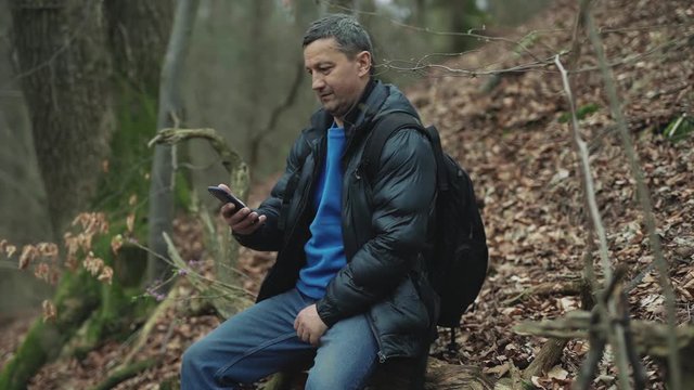 Handsome man uses smarphone in the spring forest smile feel happy technology park cellphone autumn traveller tree telephone mobile phone casual close up slow motion
