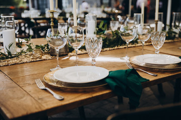 banquet wooden tables are decorated with compositions of candles and greens, on the tables are plates with napkins, glasses and cutlery. wedding, holiday