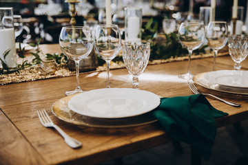 banquet wooden tables are decorated with compositions of candles and greens, on the tables are plates with napkins, glasses and cutlery. wedding, holiday