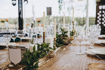 banquet wooden tables are decorated with compositions of candles and greens, on the tables are plates with napkins, glasses and cutlery. wedding, holiday