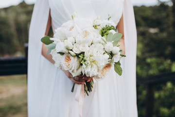 girl in a white dress holds in her hands a bouquet of white flowers and greenery with a pink...
