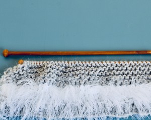 knitting needles with eyelash wool on grey and blue 