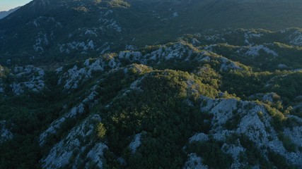 Aerial view of Montenegro rocky mountains at summer sunset. Forest on mountains. Mountainous range. Blue sky, clouds.