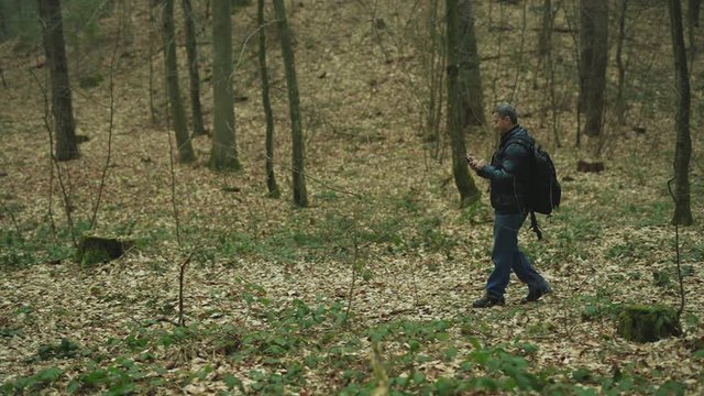 Slow motion in the forest man uses smarphone walk smile feel happy technology park cellphone autumn traveller tree telephone mobile phone casual close up