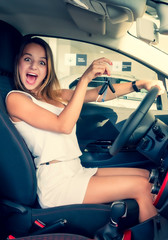 Fototapeta na wymiar Excited car driver woman smiling showing new car keys and car. Caucasian girl sitting in automobile, smiling and demonstrating keys. Female owner of vehicle. Woman is happy to purchase auto.