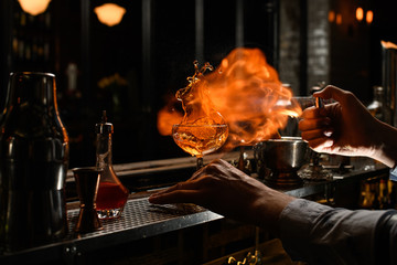 bartender with his hand holds glass with splashing drink and sets it on fire.
