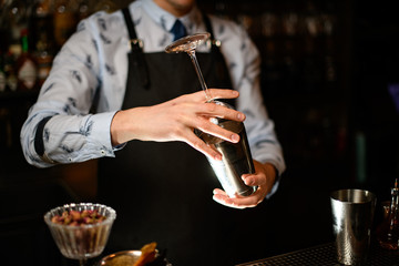 bartender holds in his hands steel shaker and empty glass