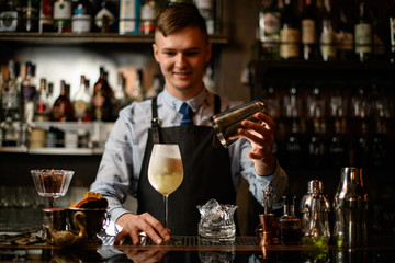 young smiling barman holds glass with ready-made cocktail