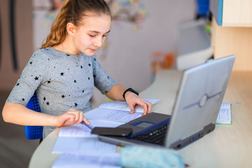 Beautiful young school girl working at home in her room with a laptop and class notes studying in a virtual class. Distance education and learning concept during quarantine