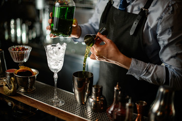Close up. Barman carefully pours green drink to steel shaker using beaker.