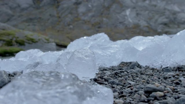 Chunks of Clear Ice Rest on a Rocky Riverbed, Close Up Slow Motion