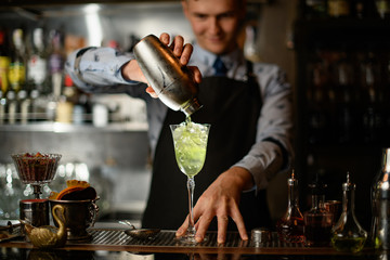 barman pours finished cocktail from shaker into glass