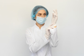 Fototapeta na wymiar A female doctor in a medical mask puts white rubber gloves