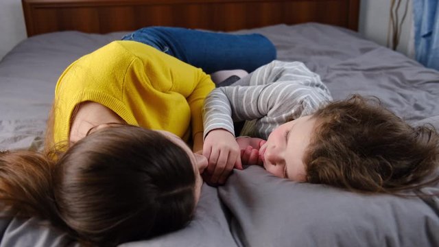 Little kid girl cuddling kissing happy young mommy lying in cozy bed, smiling mother or nanny rest take, daughter lying in bed enjoy tender moment with mom, love. Relative people family concept