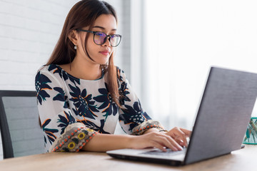 Business young woman wear glasses working typing on a laptop computer on desk at her office.