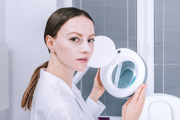 Female woman doctor is analyzing skin on face before the procedure in cabinet. Beautician...